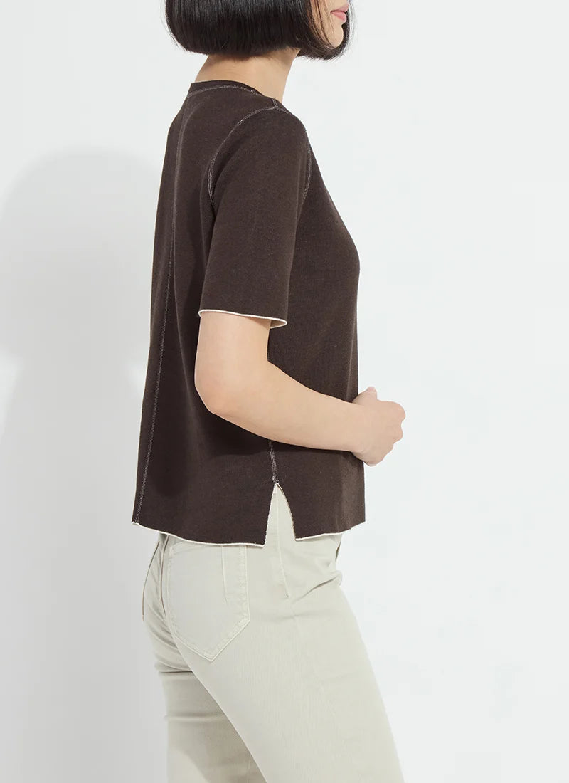 A woman shown from the side wearing a dark brown short-sleeve knit top and light beige pants, photographed against a plain white studio background.