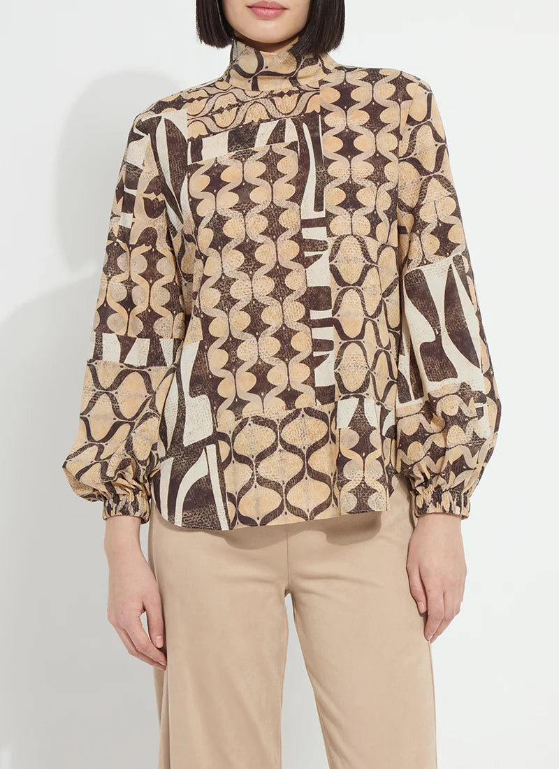 A woman wearing a beige and brown abstract patterned blouse with long balloon sleeves and beige trousers, photographed against a plain light background.